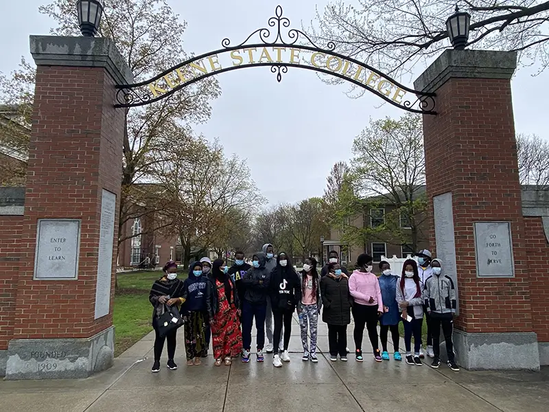a group of mixed culture people standing beneath the Keene State College campus archway