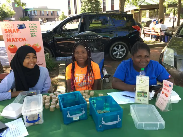 a group of 3 girls sitting at a table at a farmers market