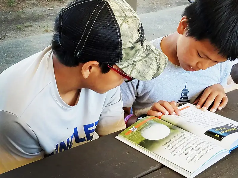 two boys reading a book at a table